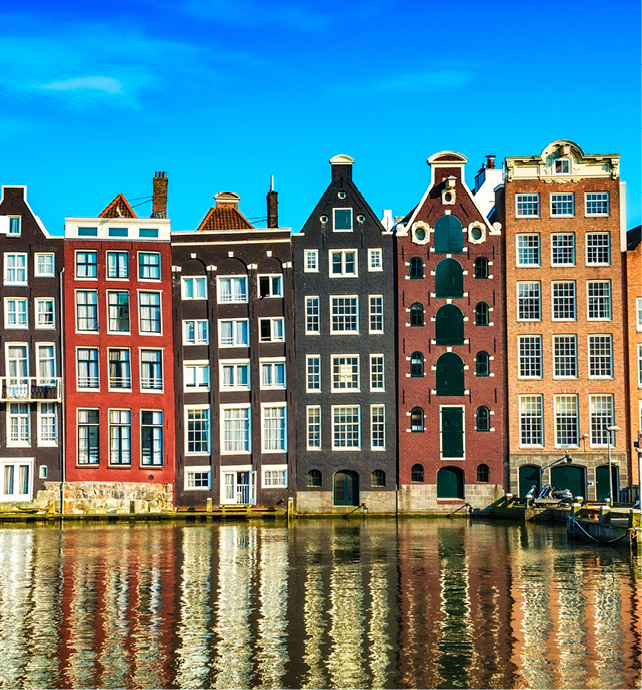 multi-coloured buildings lining the edge of the canal, with rippled reflections and boats surrounding