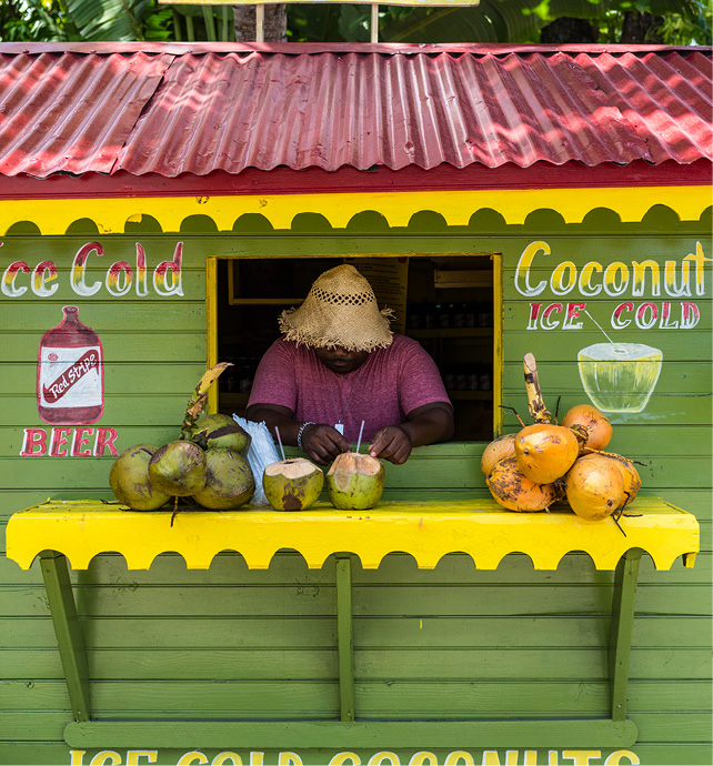 A colourful yellow, red and green stall, with a vendor selling ice cold beer, rum, and coconut drinks in the Caribbean